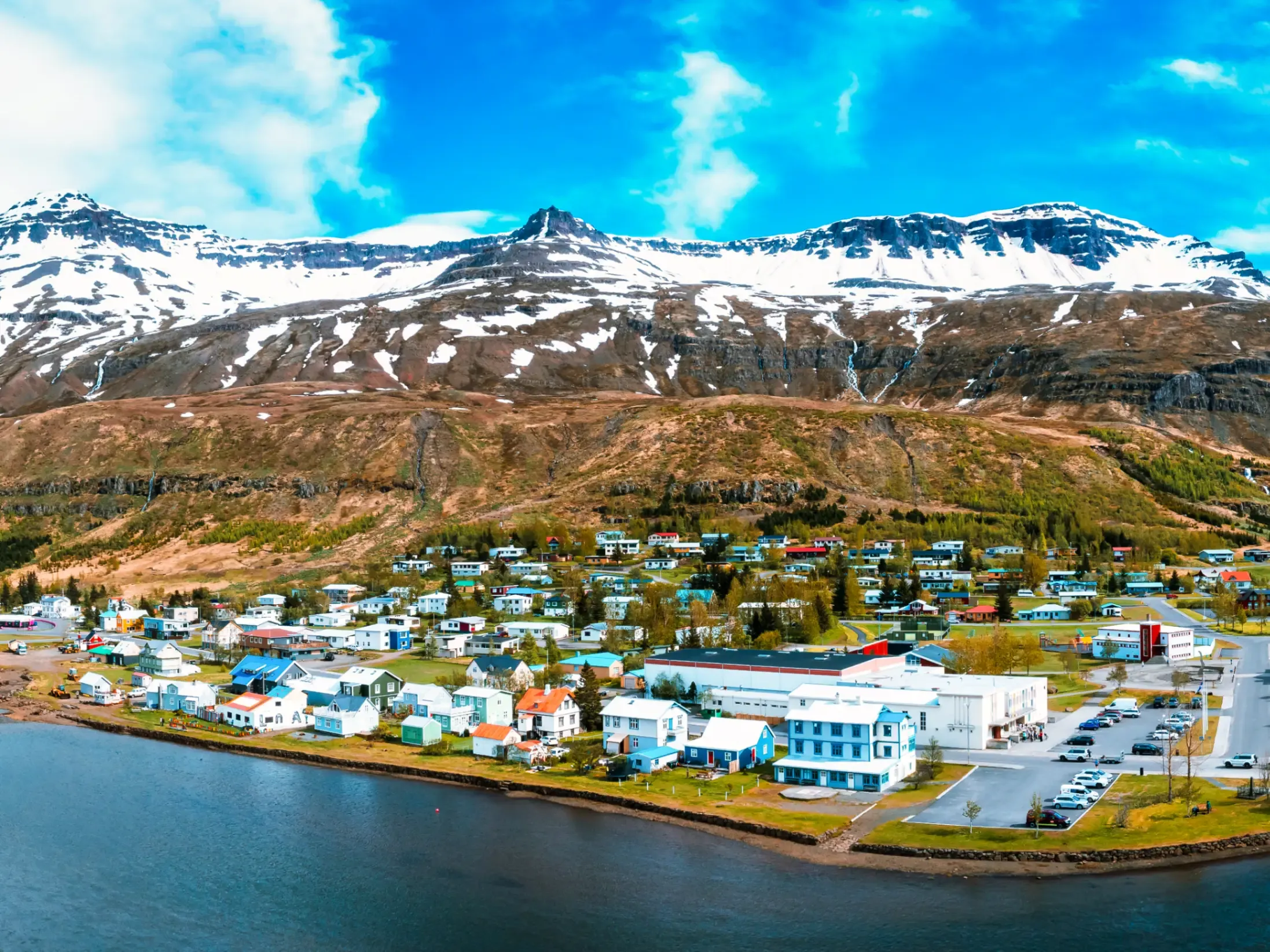 Stunning aerial view of a small town on an Icelandic peninsula surrounded by calm waters and snowy mountains.