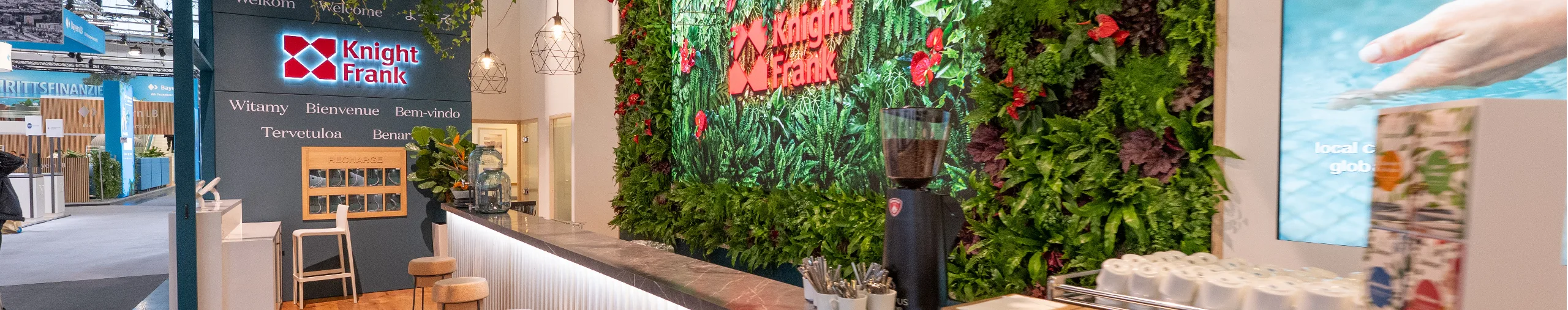 Knight Frank's exhibition stand at Expo Real, featuring a vertical garden backdrop and bench seating along a bar