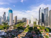 Jakarta city skyline under a bright blue sky with wispy white clouds.